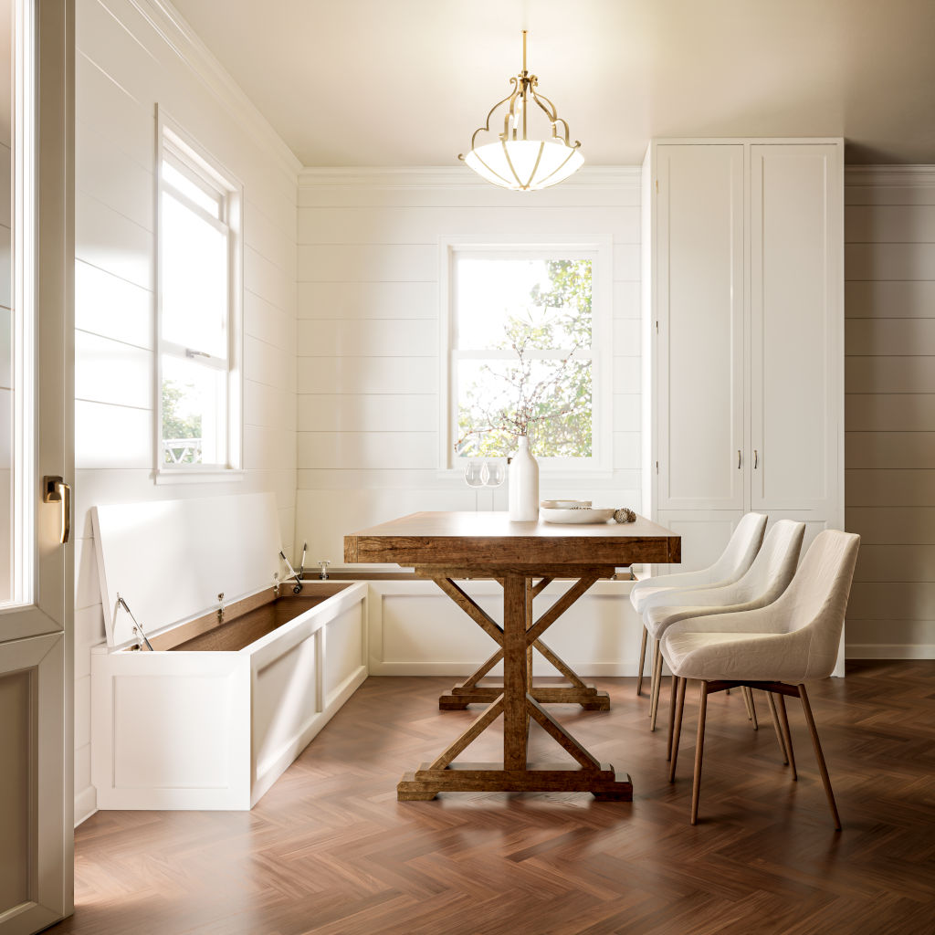 Bright dining space with an open-lid Shaker L-shaped corner bench revealing storage, paired with a robust cross-legged wooden table and chic upholstered chairs, under a classic chandelier, surrounded by warm-toned herringbone flooring and white shiplap walls.