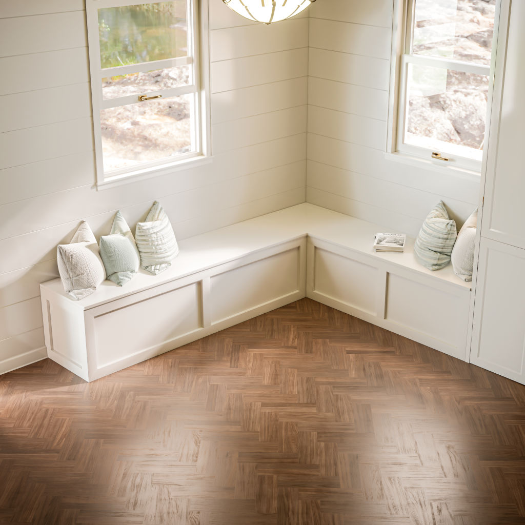Inviting corner nook with a white Shaker L-shaped bench adorned with soft decorative pillows, set against a backdrop of crisp white shiplap walls and a herringbone patterned wood floor, illuminated by natural light from surrounding windows.
