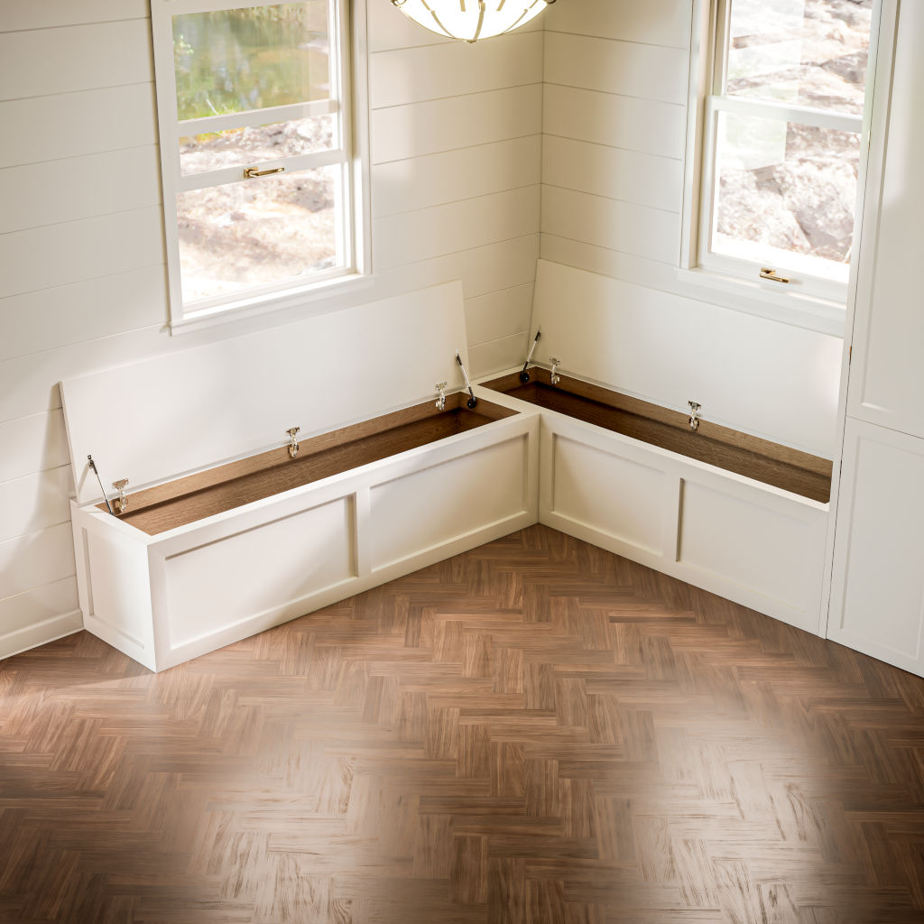 Contemporary white Shaker L-shaped corner bench with opened wooden lids revealing internal storage compartments, situated in a sunlit room with herringbone flooring and a view to the outdoors.