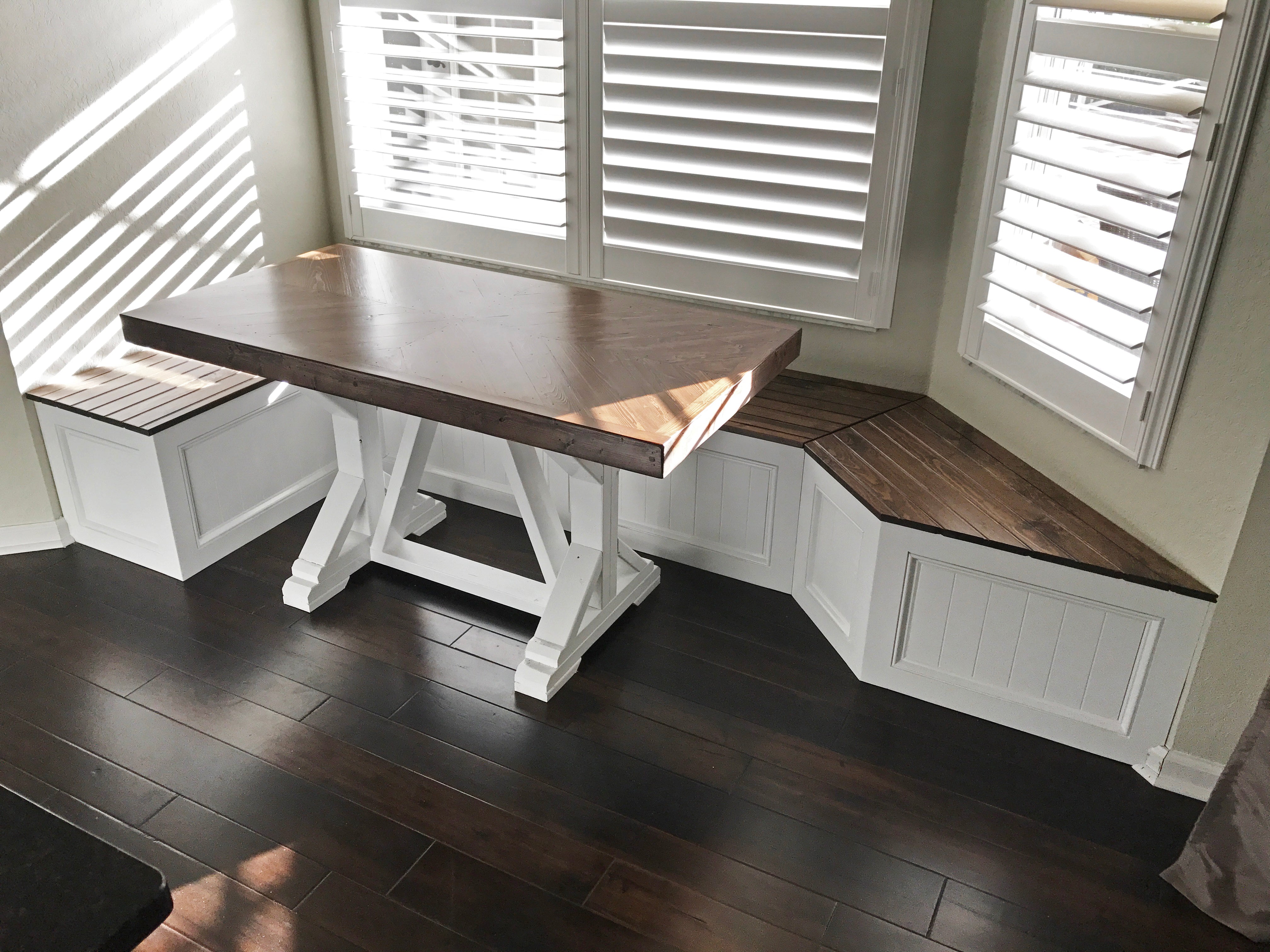 Photo of a window seat with a custom right angle on one side and a traditional window seat angle on the other side. Shown with a farmhouse herringbone top table with white painted legs